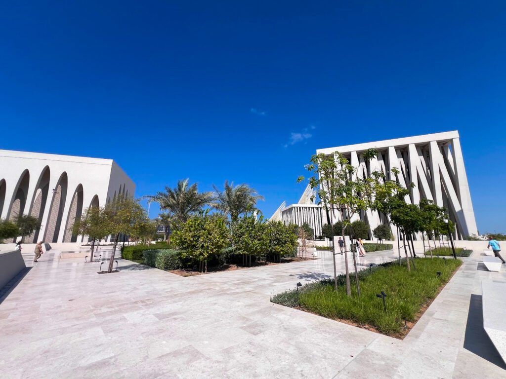 A clear blue sky backdrops a courtyard at the Abrahamic Family House between the St. Francis Church, Imam Al-Tayeb Mosque, and Moses Ben Maimon Synagogue.