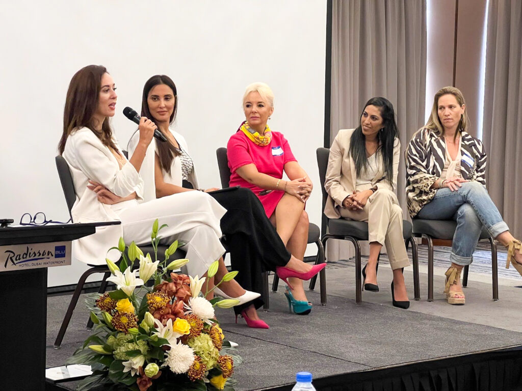 Five women on a panel discussion at the Dubai Forum look toward Nezha Alaoui, who speaks into a microphone.