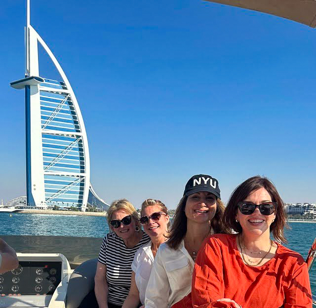 Four women from Empower Women Media's Network, pose in front of the massive sail-shaped Burj Al Arab hotel on the Dubai waterfront.